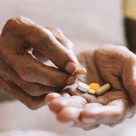 older hands holding several prescription pills