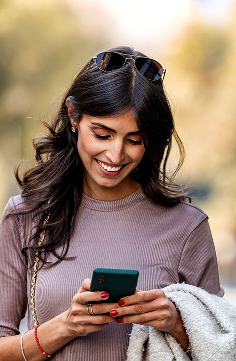 woman smiling as she reads message on her cell phone